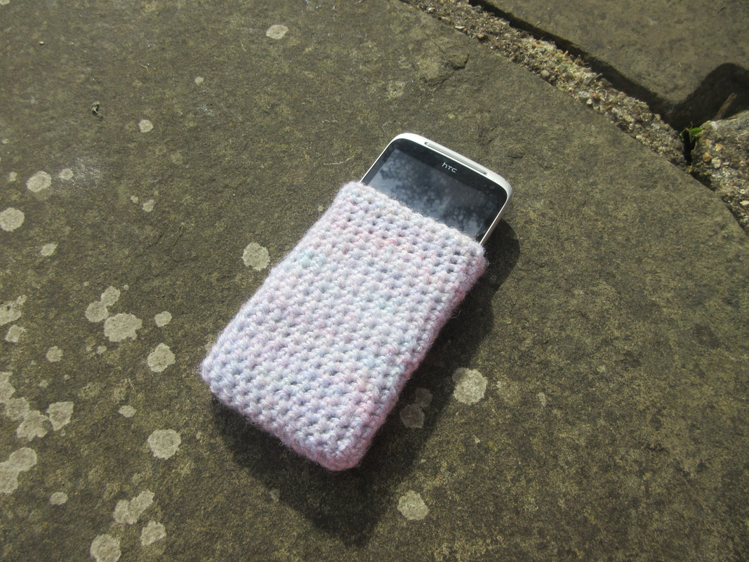 A smartphone peeking out of a crochet phone sock.