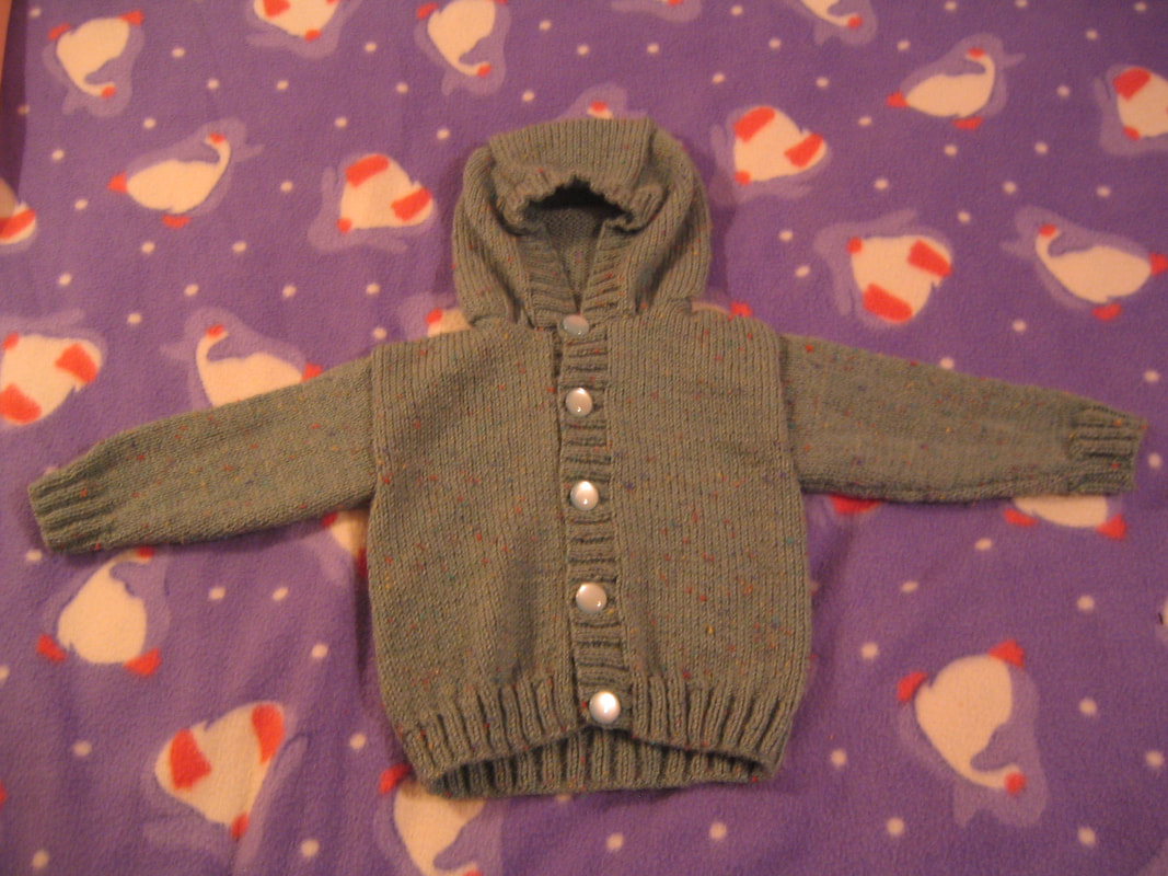 Green knitted hooded jumper with pale buttons, photographed in low light.