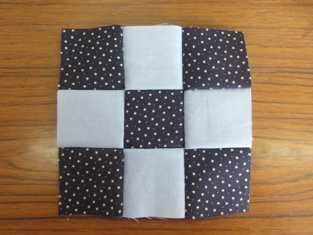 9 squares of fabric sewn in a grid formation.  The centre and corner squares are navy blue with white stars.  The other 4 squares are pale blue.