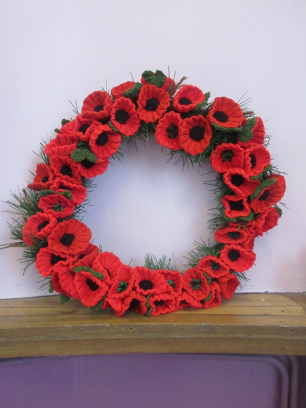 An artificial wreath, covered in bright red knitted poppies, propped up on a shelf.