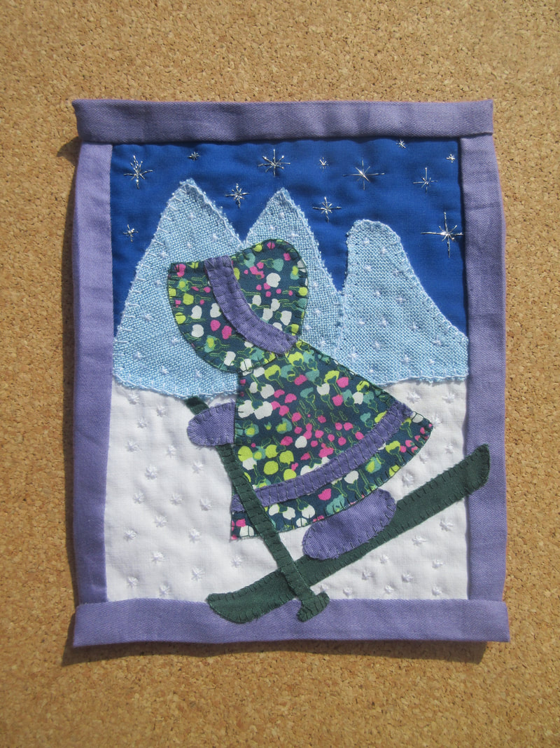Fabric collage of a girl in a floral dress and bonnet skiing down a mountain.
