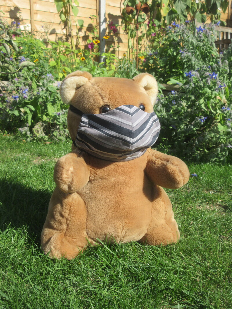 A teddy bear wearing a handmade, fabric mask over his nose and mouth.