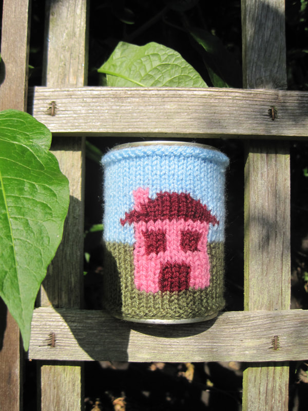 Tin can dressed in a knitted sleeve.  The picture knitted into the sleeve is a simple house with a door, two windows and a chimney.  The windows are solid blocks.