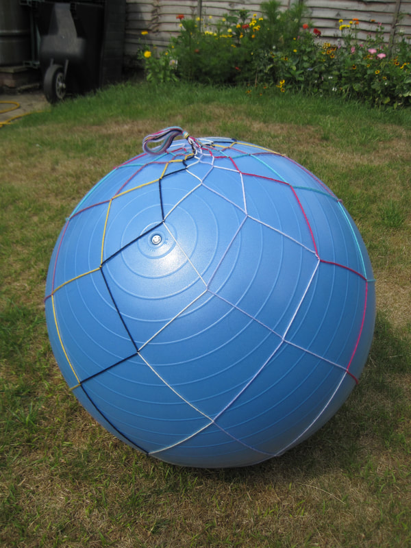 Large blue exercise ball with a net of multicoloured yarn around it.